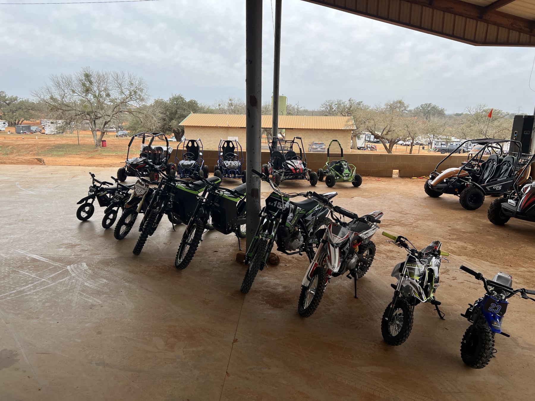 Youth dirt bikes and go-karts lined up under a covered pavilion at a Hill Country track